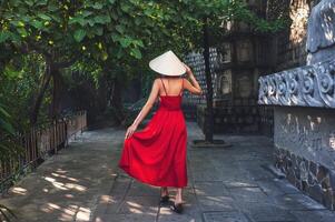 A tourist in a red dress and a traditional Vietnamese hat in the garden of a pagoda in Asia photo