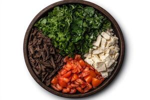 Overhead shot of a delicious and healthy mediterranean salad with chopped tomatoes, feta cheese, shredded beef, and fresh greens in a rustic wooden bowl photo