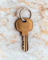 Close up of a gold key with a silver keyring on a marble surface photo