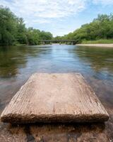 Rustic wooden platform in shallow river with old bridge in background photo