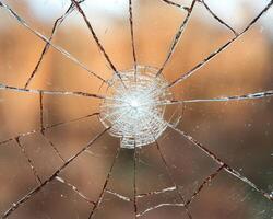 Close up of a shattered window with a central impact point, showing radial cracks and fragmentation photo