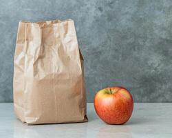 Brown paper lunch bag and red apple on a grey background photo