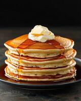 A stack of fluffy pancakes drizzled with syrup and topped with butter photo
