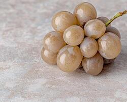 Close up of a cluster of ripe, pale beige grapes on a light beige textured surface photo