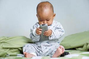 The little Asian girl under 3 year old had just woken up and was sitting on the bed playing with the remote. photo