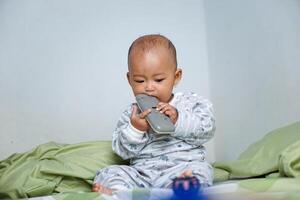 The little Asian girl under 3 year old had just woken up and was sitting on the bed playing with the remote. photo