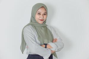 A confident asian woman in a green hijab poses with arms crossed, showcasing strength and elegance. photo