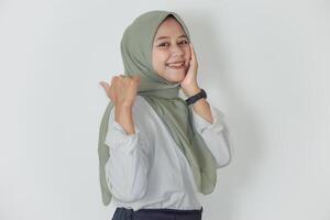 A young asian woman in a green hijab smiles confidently, showcasing positivity and charm. photo