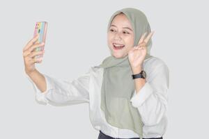 A smiling asian woman in a hijab enjoys a call photo