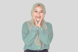 A joyful asian woman in a green outfit and hijab smiles brightly, expressing happiness and warmth. photo