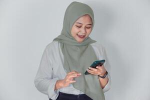 An Asian woman in a green hijab smiles while using her smartphone, showcasing modern communication. photo