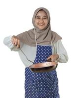 A woman in a hijab and a polka dot apron joyfully cooks with a frying pan, embodying the delight and warmth of home-cooked meals. photo