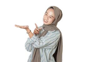A woman in a striped shirt and brown hijab smiling and pointing at her open hand, suggesting something or presenting an idea, against a white background. photo