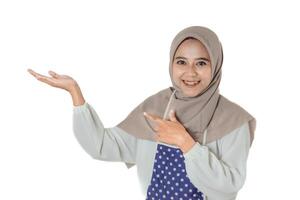 A woman wearing a gray headscarf and polka-dot apron smiles while pointing and extending her hand, showing or exposing something. photo
