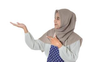 A woman wearing a gray headscarf and polka-dot apron smiles while pointing and extending her hand, showing or exposing something. photo