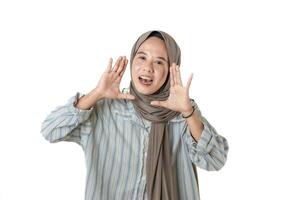 A woman wearing a hijab and striped shirt smiles while making a cheerful gesture, appearing to be calling out or speaking enthusiastically. photo