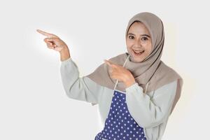 A woman wearing a gray headscarf and polka-dot apron smiles while pointing and extending her hand, showing or exposing something. photo