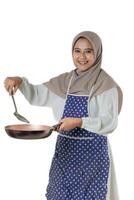 A woman in a hijab and a polka dot apron joyfully cooks with a frying pan, embodying the delight and warmth of home-cooked meals. photo