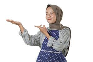 A woman wearing a gray headscarf and polka-dot apron smiles while pointing and extending her hand, showing or exposing something. photo