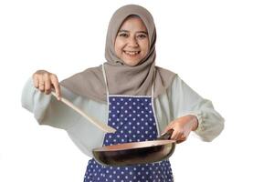 A woman in a hijab and a polka dot apron joyfully cooks with a frying pan, embodying the delight and warmth of home-cooked meals. photo