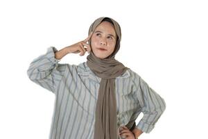 A woman wearing a gray hijab and a striped shirt touches her temple while looking thoughtful, as if she is contemplating an idea or decision. photo