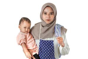 A woman in a hijab and apron holds a child, with a determined expression, merging nurturing and duty, symbolizing the strength and love of motherhood. photo