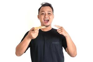 Happy Asian Man Pointing at a Delicious Slice of Pizza in Hand photo