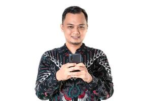 Man Smiling and Using Smartphone in Traditional Batik Shirt photo