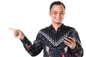 Man in Batik Shirt Pointing While Holding a Smartphone with a Cheerful Smile photo