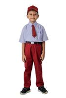 A Indonesian young boy in a school uniform smiles confidently. He wears a red cap, red tie, and red pants. photo
