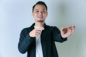 A smiling man in a black shirt and white undershirt is pointing to his open palm, as if presenting or showcasing something against a plain background. photo