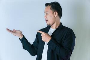 A man in a black shirt confidently points to his open palm, indicating or hinting at something against the blank white background. photo