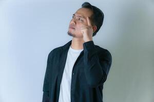 A man in a black shirt and white t-shirt deep in thought. He looks upward with his finger on his temple, as if pondering or planning something. photo