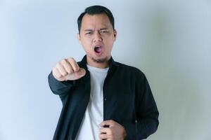 A man in a black shirt and white t-shirt yells while thrusting his fist forward, expressing determination or aggression against a plain background. photo