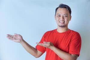 A man in a red shirt smiles while pointing to his left with both hands, presenting or accentuating something against a plain white background. photo