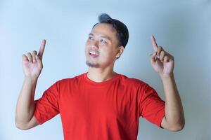A man in a red shirt is smiling and pointing upwards with both index fingers, looking cheerful and excited. isolated on white background photo