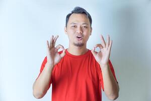 A man in a red shirt with both of his hand giving an OK hand gesture with a smile, indicating satisfaction or approval. photo