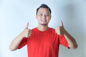 A man in a red shirt is smiling and giving two thumbs up, showing a gesture of positivity and approval against a plain white background. photo