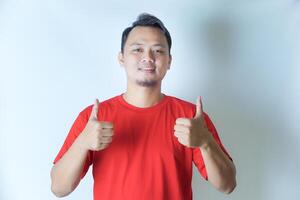 A man in a red shirt is smiling and giving two thumbs up, showing a gesture of positivity and approval against a plain white background. photo
