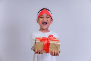 A joyful child wearing a headband, smiling widely while holding a gift wrapped with red ribbon. photo