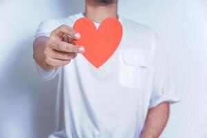 A person holds up a red heart-shaped cutout, symbolizing love and affection against a clean white background. World Heart Day concept photo
