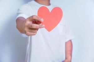 A person holds up a red heart-shaped cutout, symbolizing love and affection against a clean white background. World Heart Day concept photo