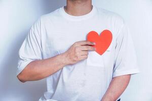 A person holds a red paper heart close to their chest, symbolizing love and affection against a soft background. World Heart Day concept photo