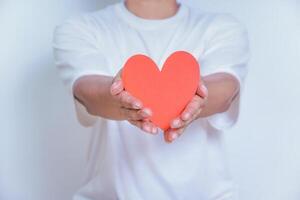 A person holds up a red heart-shaped cutout, symbolizing love and affection against a clean white background. World Heart Day concept photo