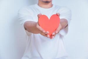 A person holds up a red heart-shaped cutout, symbolizing love and affection against a clean white background. World Heart Day concept photo