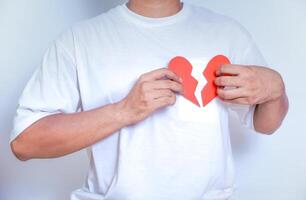 A person holds two red paper halves of a heart, symbolizing heartbreak and emotional pain, against a white background. photo