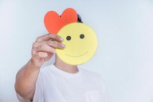A person holds a smiling face and a heart, symbolizing happiness and love in a simple yet expressive way. photo