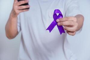 A person holds a purple ribbon in one hand while using a smartphone, symbolizing awareness and support. Healthcare and World cancer day concept photo