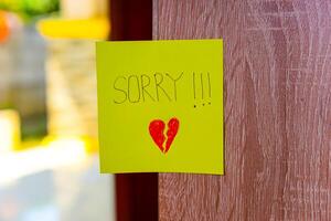 A heartfelt note on a yellow sticky note expresses deep remorse with a broken heart drawing. photo