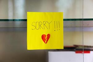 A heartfelt note on a yellow sticky note expresses deep remorse with a broken heart drawing. photo